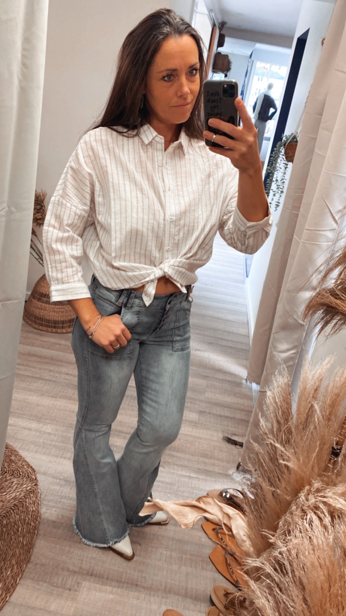 Rory Blouse, witte blouse met beige strepen en 7/8 mouwen gecombineerd met lichtblauwe flared jeans en witte laarzen.