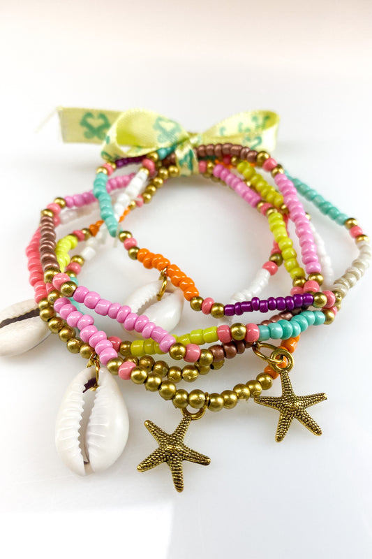 Set van 5 kleurrijke bohemian armbanden van Hot Lava met gouden accenten, schelp en zeester hanger. Ibiza- style met tropische vibes, perfect voor een zomerse look.