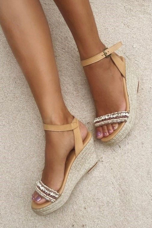 Sandalen Lanai Indy van Hot Lava. Luxueuze afwerking aan de band over de tenen, deze is met steentjes bezet in witte en beige naturelle kleuren. De schoen heeft een sluiting met gesp aan de enkel. De zool bestaat uit een plateau sleehak, bewerkt met gevlochten touw.