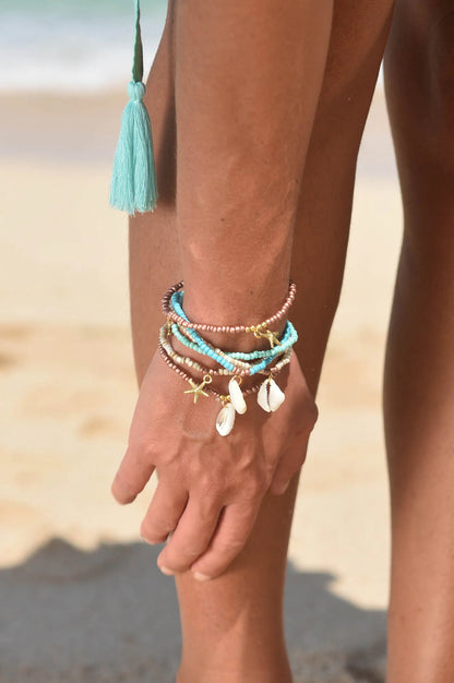 Set van 5 Belize armbanden van Hot Lava - handgemaakte sierraden met schelpen, zeester bedels in aardetinten, turquoise en gouden accenten.
